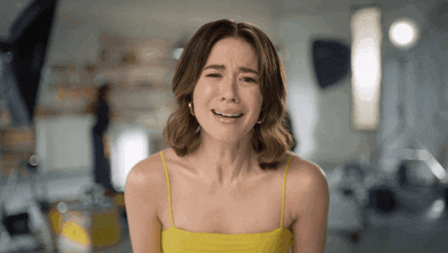 a woman in a yellow top is crying with her eyes closed