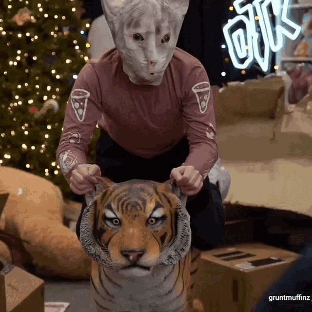 a person wearing a cat mask sits on a stuffed tiger head