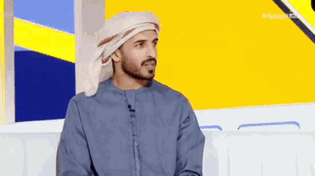 a man wearing a head scarf is sitting on a couch with a yellow background