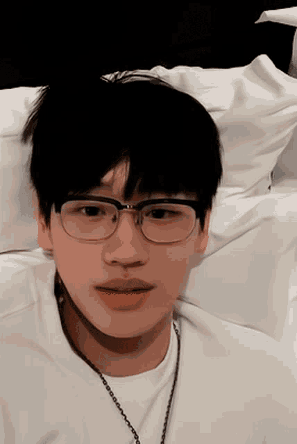 a young man wearing glasses and a necklace laying on a bed