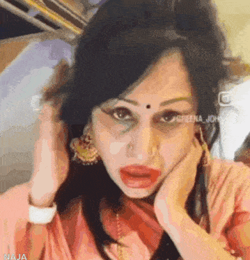 a woman with a nose ring is wearing a pink shirt and gold earrings