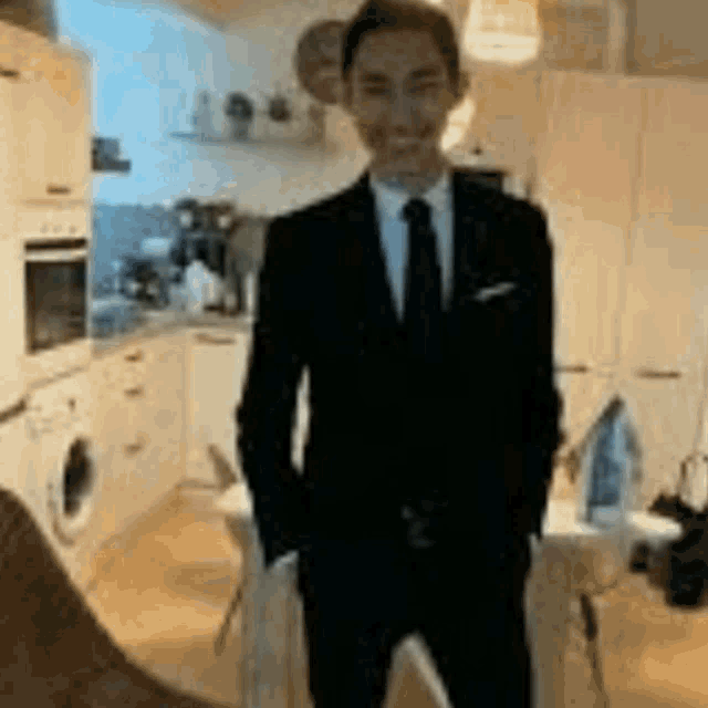 a man in a suit and tie standing in a kitchen with his hands in his pockets .