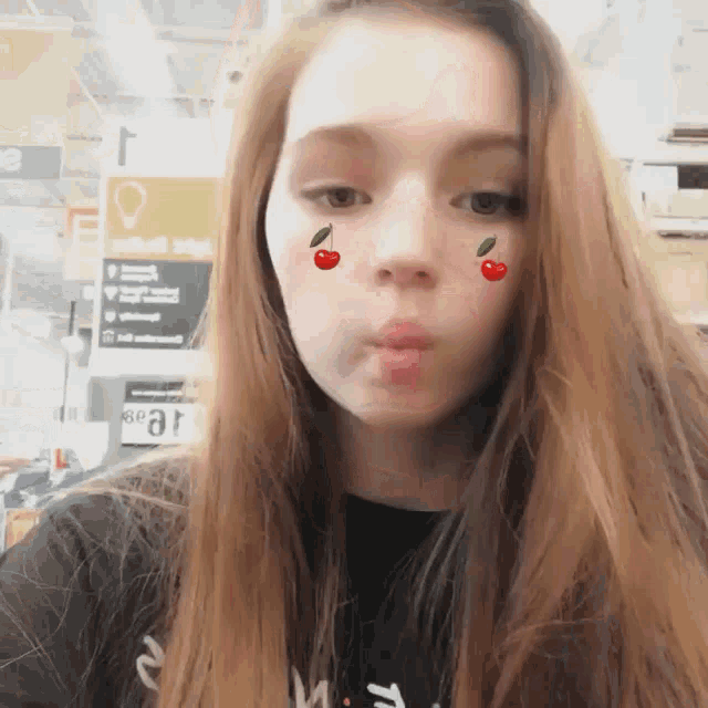 a girl wearing a black shirt with the letter m on it makes a face with cherries on her face