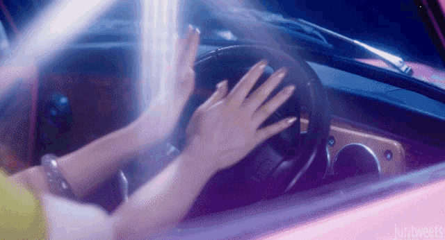 a woman is driving a pink car and touching the steering wheel with her hands .