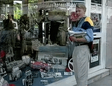 a man is standing in front of a store window holding a newspaper .