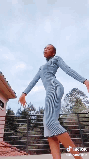 a woman in a blue dress is standing on a balcony with her arms outstretched and a tiktok watermark on the bottom