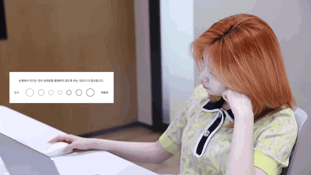 a woman with red hair sits at a desk next to a sign that says ' o ' on it