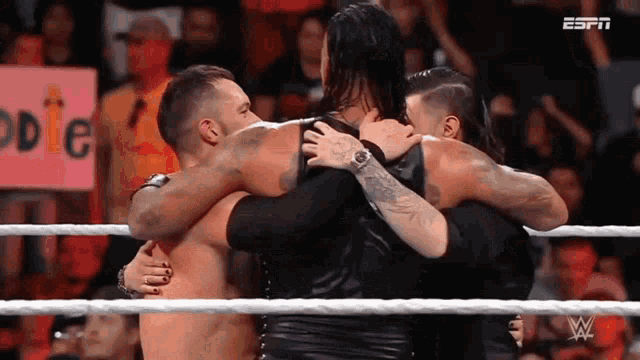 three wrestlers are hugging each other in a wrestling ring .