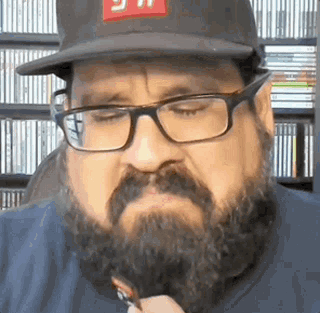 a man with a beard and glasses is wearing a hat and smoking a cigarette .