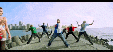 a group of young men are dancing on a pier near the ocean .