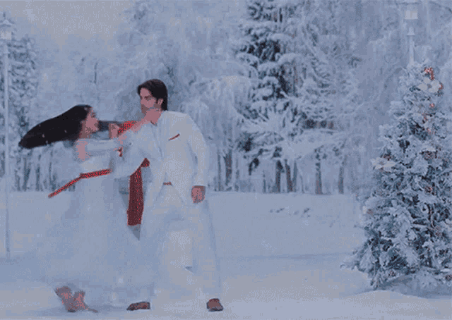a man and woman are dancing in the snow with a christmas tree in the background