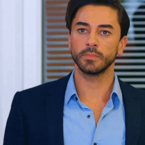 a man with a beard is wearing a blue shirt and a black jacket