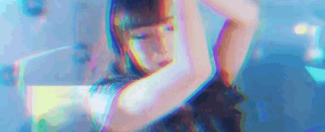 a woman is dancing in a dark room with a rainbow of colors behind her .