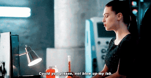 a woman is sitting at a desk with a lamp and a bottle of liquid and says could you please not blow up my lab