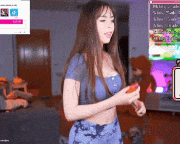 a woman in a blue top and tie dye pants is standing in a living room holding a remote control .