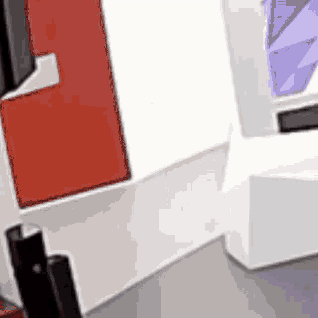 a blurred image of a room with a white wall , a red door , and a purple box .