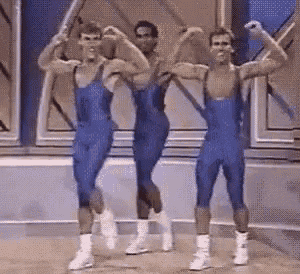 three men in blue leotards are dancing on a stage and flexing their muscles .