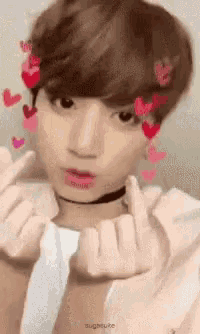 a young man with hearts in his hair is making a heart shape with his fingers .