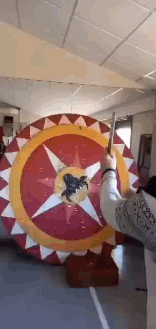 a person is holding a sword in front of a large circular target with a horse on it .