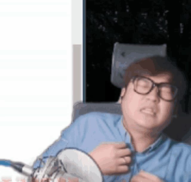 a man wearing glasses and a blue shirt is sitting in front of a microphone