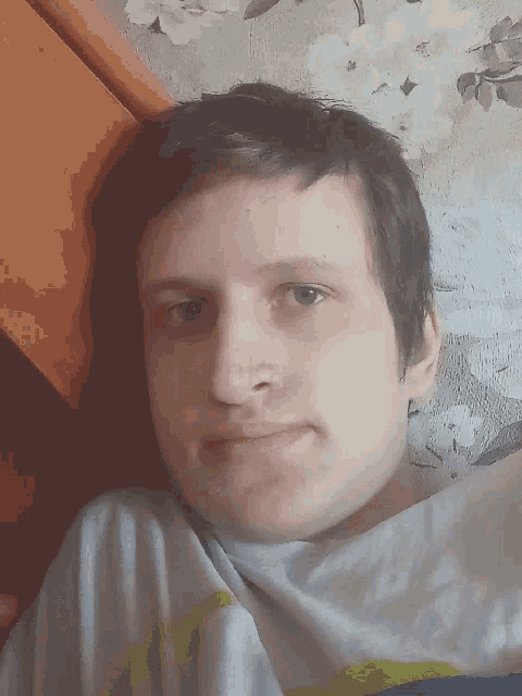 a young man is laying on a bed with a floral wallpaper behind him