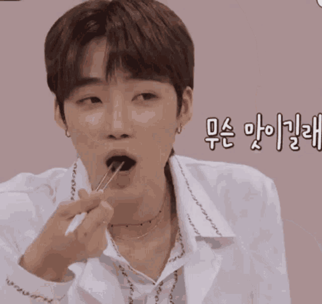a man in a white shirt is eating something with chopsticks with korean writing behind him