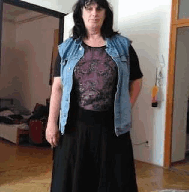 a woman wearing a denim vest and a black skirt is standing in a room .