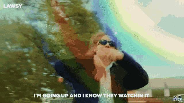 a man wearing sunglasses and a suit says " i 'm going up and i know they watchin it "