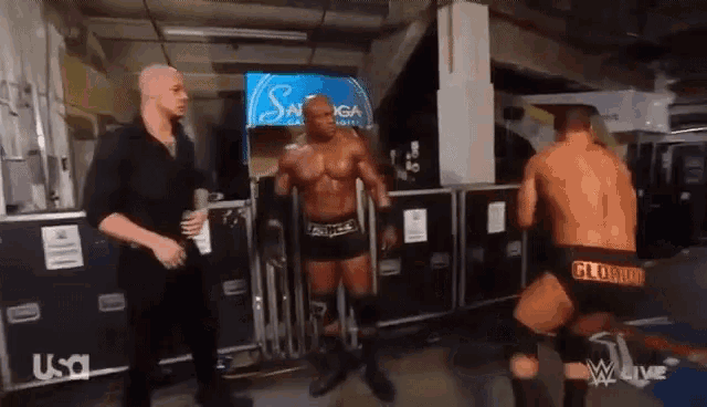 two wrestlers are standing in a room with a sign that says savings on it