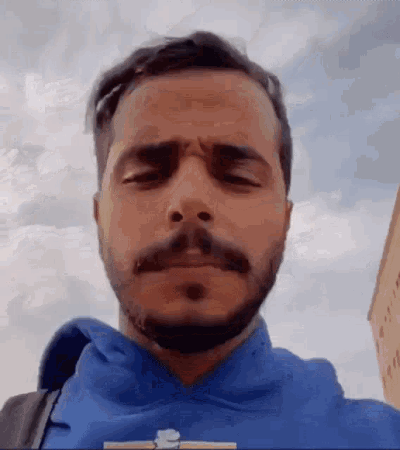 a man with a beard is wearing a blue hoodie .