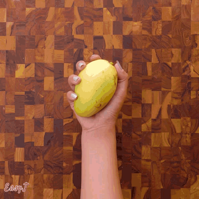 a woman 's hand is holding a mango on a wooden cutting board with easy j written on the bottom right