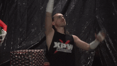 a man in a xmas wrestler shirt is dancing in front of a christmas tree