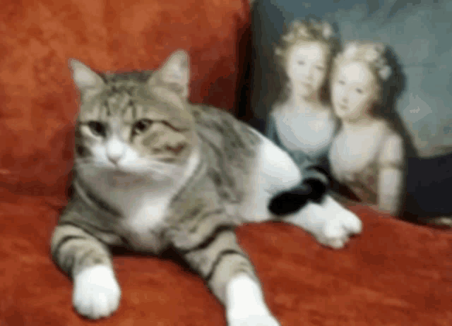 a cat is laying on a red couch next to a pillow with a picture of two girls on it