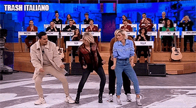 a group of people are dancing on a stage in front of a crowd with the words trash italiano above them .