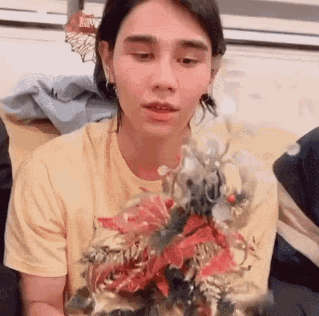 a young man in a yellow shirt is holding a christmas tree in his hand .