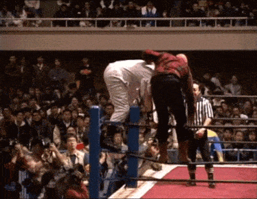 a referee stands in a wrestling ring watching a wrestler climb the ropes