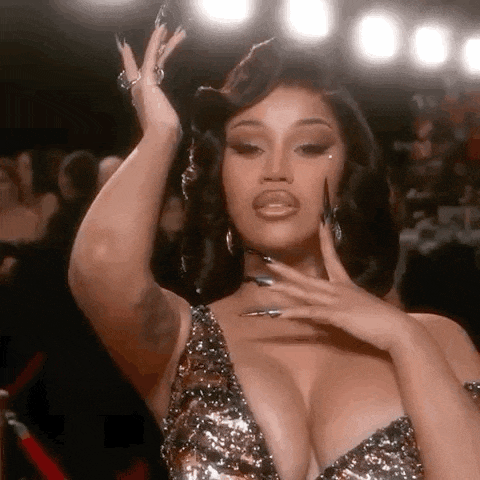 cardi b is wearing a very revealing dress with a plunging neckline and very long nails .