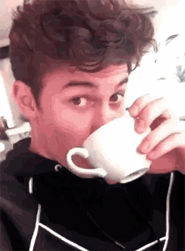 a young man with curly hair is drinking a cup of coffee .