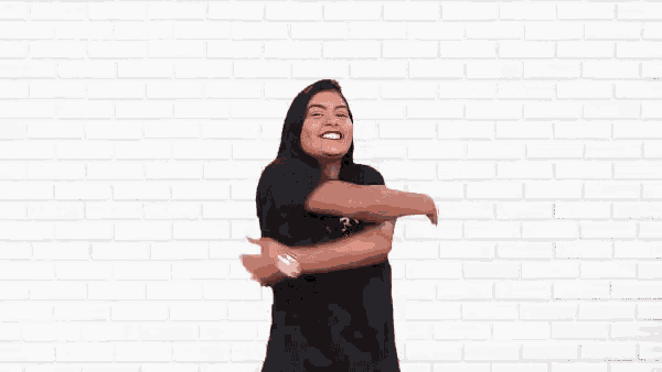 a woman wearing a black shirt is dancing in front of a white brick wall .
