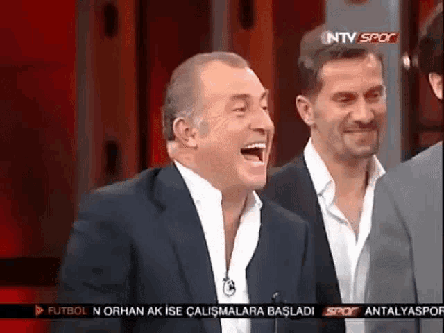 two men are laughing in front of a tv screen that says antalyaspor