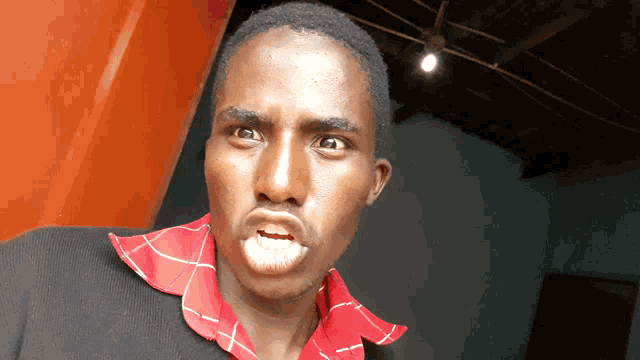 a man wearing a black sweater and a red and white checkered shirt makes a funny face