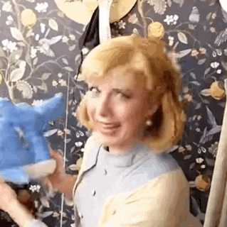 a woman is holding a blue stuffed animal in front of a wall with flowers on it .