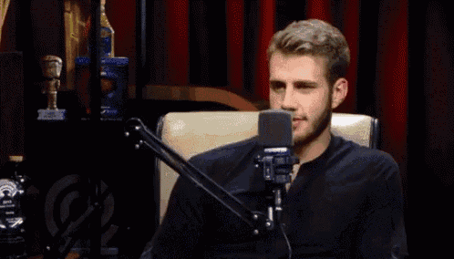 a man in a black shirt is sitting in front of a microphone and smiling .