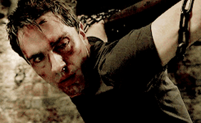 a man is chained to a wall and has blood on his face