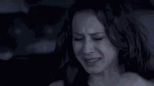 a woman is sitting in a car with her eyes closed and her hand on her head .