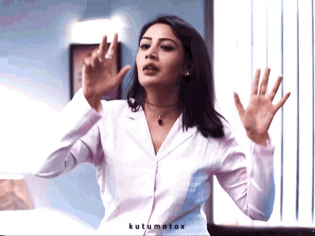 a woman in a white shirt is standing in front of a window with the words kutumotox on the bottom right