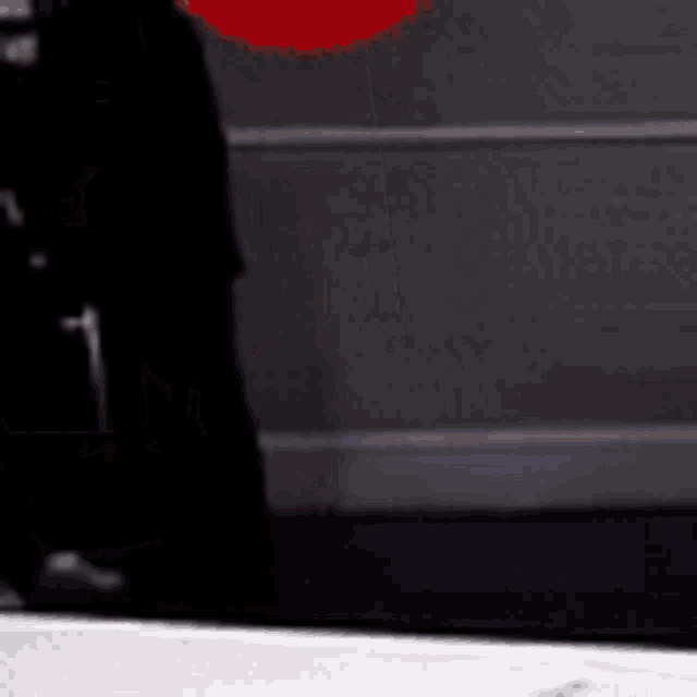 a man in a black suit is holding a red umbrella in front of a wall .