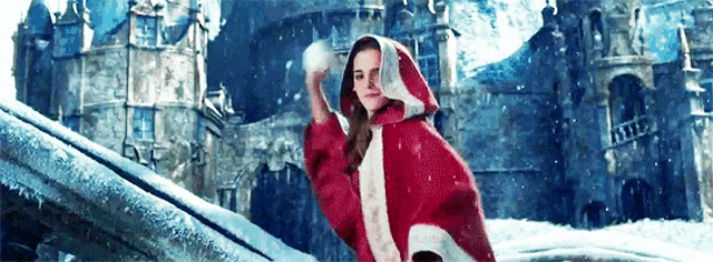 a woman in a red cape is throwing a snowball in the air .
