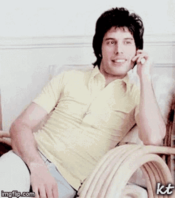 a man in a yellow shirt is sitting in a chair and talking on a cell phone ..