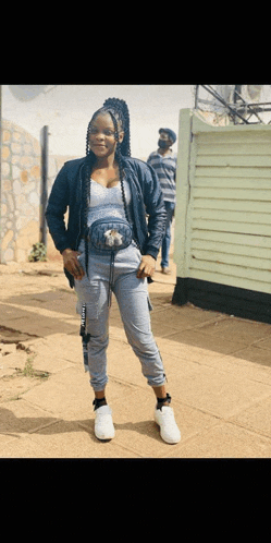 a woman is standing on a sidewalk wearing a blue jacket and grey sweatpants .